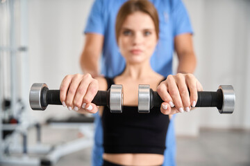 Woman performs exercises with dumbbells under the supervision of physiotherapist