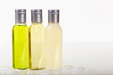Three small bottles with cosmetics on light background with white petals. Shampoo, shower gel, body lotion. Travels, tourism, hotels. Natural organic cosmetics. Body care