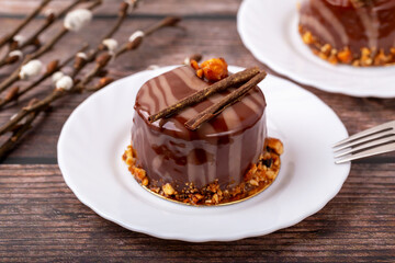 Fresh delicious chocolate souffle cake on white plate on wooden background. Caramel glaze and decoration add appeal and desire. Willow twigs lie nearby. Easter