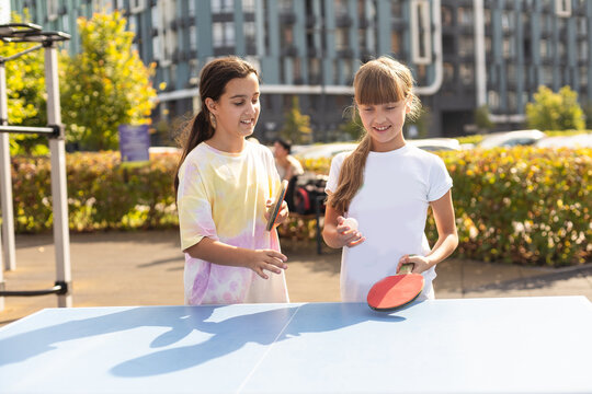 Young teenager girl playing ping pong. She holds a ball and a racket in her hands. Playing table tennis outdoors in the yard