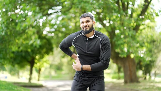 Adult bearded runner experiences a sharp pain in his right side during a morning run in a park. The male has a liver bolt. The sportsman gasps in pain, clutching his side as he slows down his pace