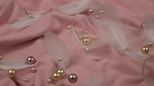 White and pink pearl beads fall on the   pink velvet with swan feathers laying on it, slow motion 