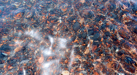 Detail of cobblestones in the transparent water of the famous Red Beach, Santorini. Background, natural stone, texture.