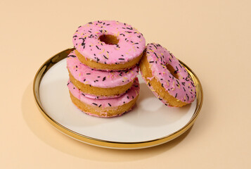 Donut covered with pink glaze and sprinkled with colorful sprinkles on a round plate, brown background