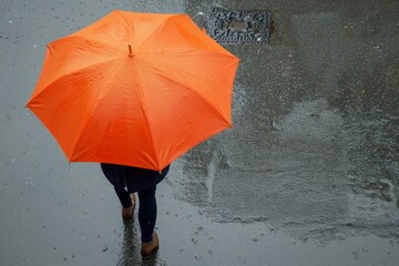 Orange Umbrella on Wet Urban Street - Overhead view of an individual with an orange umbrella, walking alone on a rainy city street.