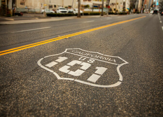 Highway 101 sign painted on the black asphalt road with city diffused in the background. The shot...