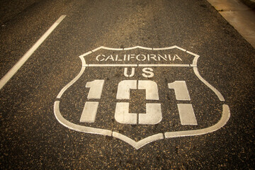 Highway 101 sign painted on the black asphalt road with city diffused in the background. The shot...