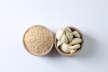Dehydrated garlic granules and peeled cloves on white table, flat lay