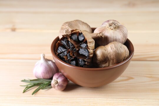 Bulbs of fresh and fermented black garlic on wooden table
