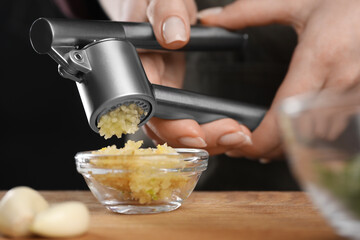 Woman squeezing garlic with press at wooden table, closeup