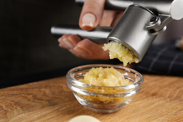 Woman squeezing garlic with press at wooden table, closeup