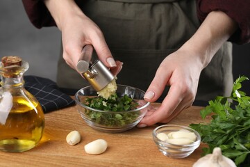 Woman squeezing garlic with press at wooden table, closeup