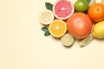 Different cut citrus fruits and leaves on beige table, flat lay. Space for text