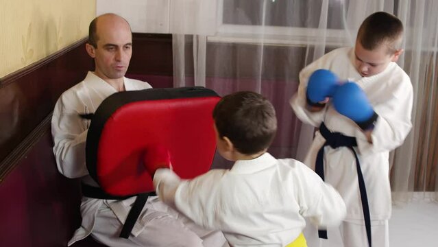 A boy with red pads on his hands actively punches the simulator in the hands of a trainer