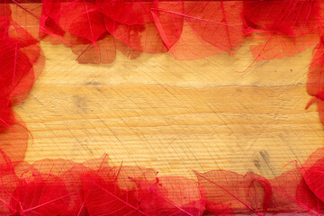frame of red painted leaves on wooden background with space for text