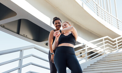 Two smiling female athletes looking at the smartwatch. Plus size female showing her fitness friend...
