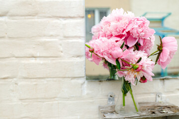 Bouquet of peonies near mirror outdoors near white brick wall