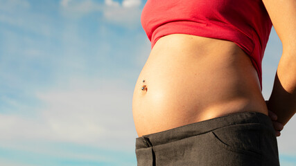 pregnancy expecting baby showing proud belly with a background of light blue sky and red t-shirt...