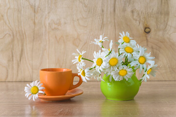 Summer morning breakfast concept; orange cup of coffee and bouquet of white daisies on a wooden...