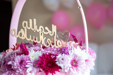 Pink Bouquet with heart shape and multi colors and balloons in the background as decoration for celebrationwith arabic word translation : الحمدلله على السلامة (Thank god for safty)