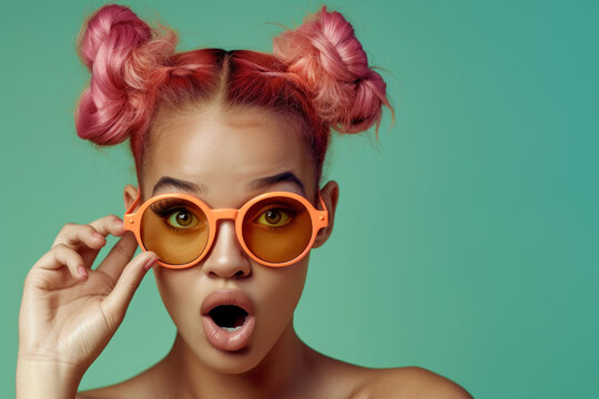 Surprised funny girl wearing glasses with round frames. a girl with pink hair with pigtails and two buns. The girl's mouth is open in surprise and her hands are holding her glasses. on a green back