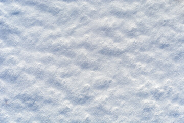 Uneven lumpy snow surface. Pressed snow melted in the sun. White and blue texture or abstract winter background