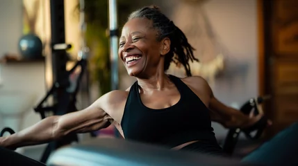 Rolgordijnen Professional Portrait of an active black African American mature woman smiling and doing fitness pilates and strength resistance training at her home gym. Candid senior female exercising at home © Sophie