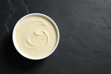 Tasty melted white chocolate in bowl on black table, top view. Space for text