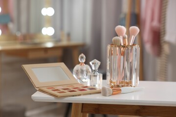 Set of brushes, eyeshadow palette and perfumes on white table in makeup room