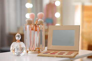 Set of brushes, eyeshadow palette and perfume on white table in makeup room