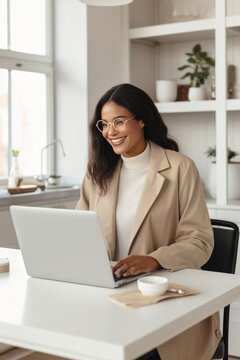 Smiling young African woman, in glasses and in beige clothes using a laptop, work online, at a distance, vertical image
