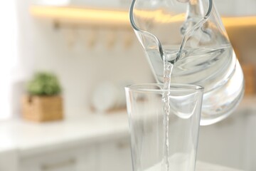 Pouring water from jug into glass in kitchen, closeup. Space for text