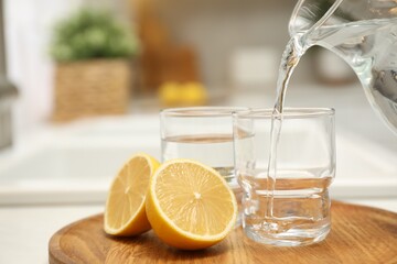 Pouring water from jug into glass on table in kitchen, closeup. Space for text
