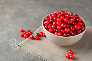 Cranberries in bowl on light grey table, closeup. Space for text
