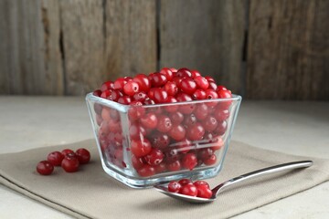 Cranberries in bowl and spoon on light grey table, closeup