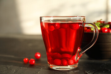 Tasty hot cranberry tea in glass cup and fresh berries on black textured table