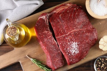 Fresh raw beef cuts with oil and spices on wooden table, top view