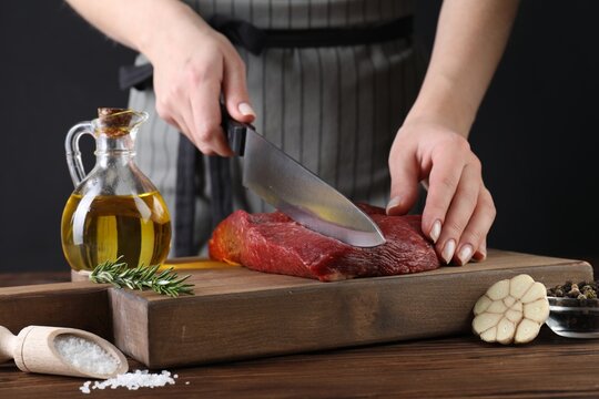 Woman cutting fresh raw beef steak at wooden table, closeup
