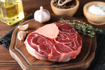 Piece of raw beef meat, garlic and thyme on wooden table, closeup
