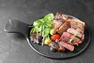 Delicious grilled beef meat, vegetables and greens on black table