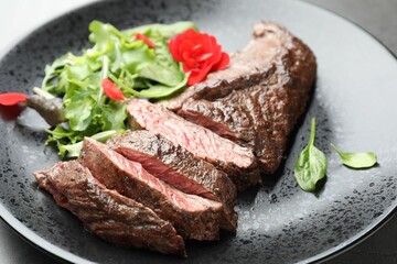 Pieces of delicious grilled beef meat and greens on table, closeup