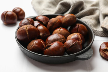 Fresh edible sweet chestnuts in frying pan on white tiled table, closeup