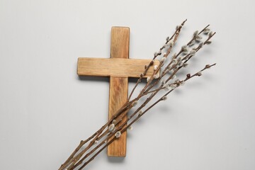Wooden cross and willow branches on light grey background, top view. Easter attributes