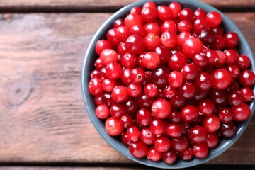 Fresh ripe cranberries in bowl on wooden table, top view
