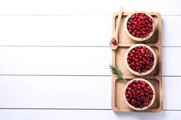 Fresh ripe cranberries in bowls and rosemary on white wooden table, top view. Space for text