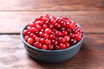 Fresh ripe cranberries in bowl on wooden table, closeup