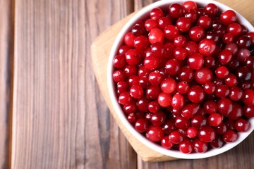 Fresh ripe cranberries in bowl on wooden table, top view. Space for text