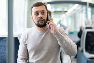 Portrait of european man standing in tram carriage and using his phone