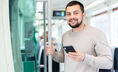 Fototapeta na wymiar Relaxed young bearded man using his smartphone during trip in public transport ..