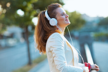 smiling stylish woman in city listening to music